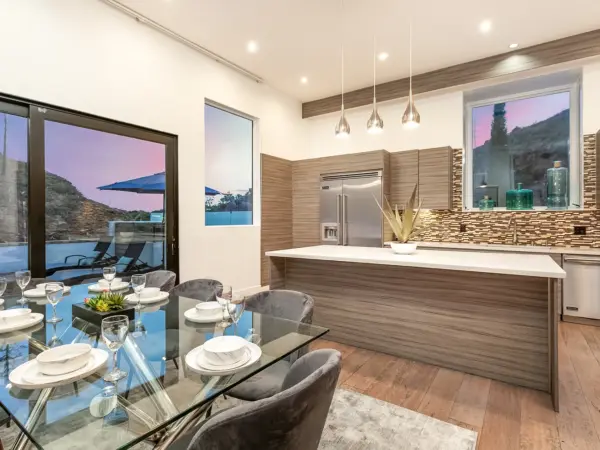 Glass-top dining table in front of large window and modern kitchen island.